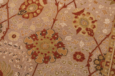 A close-up of a traditional patterned rug featuring large floral medallions and delicate leafy vines in rust red, beige, ochre yellow, and muted green on a dusty pink background.